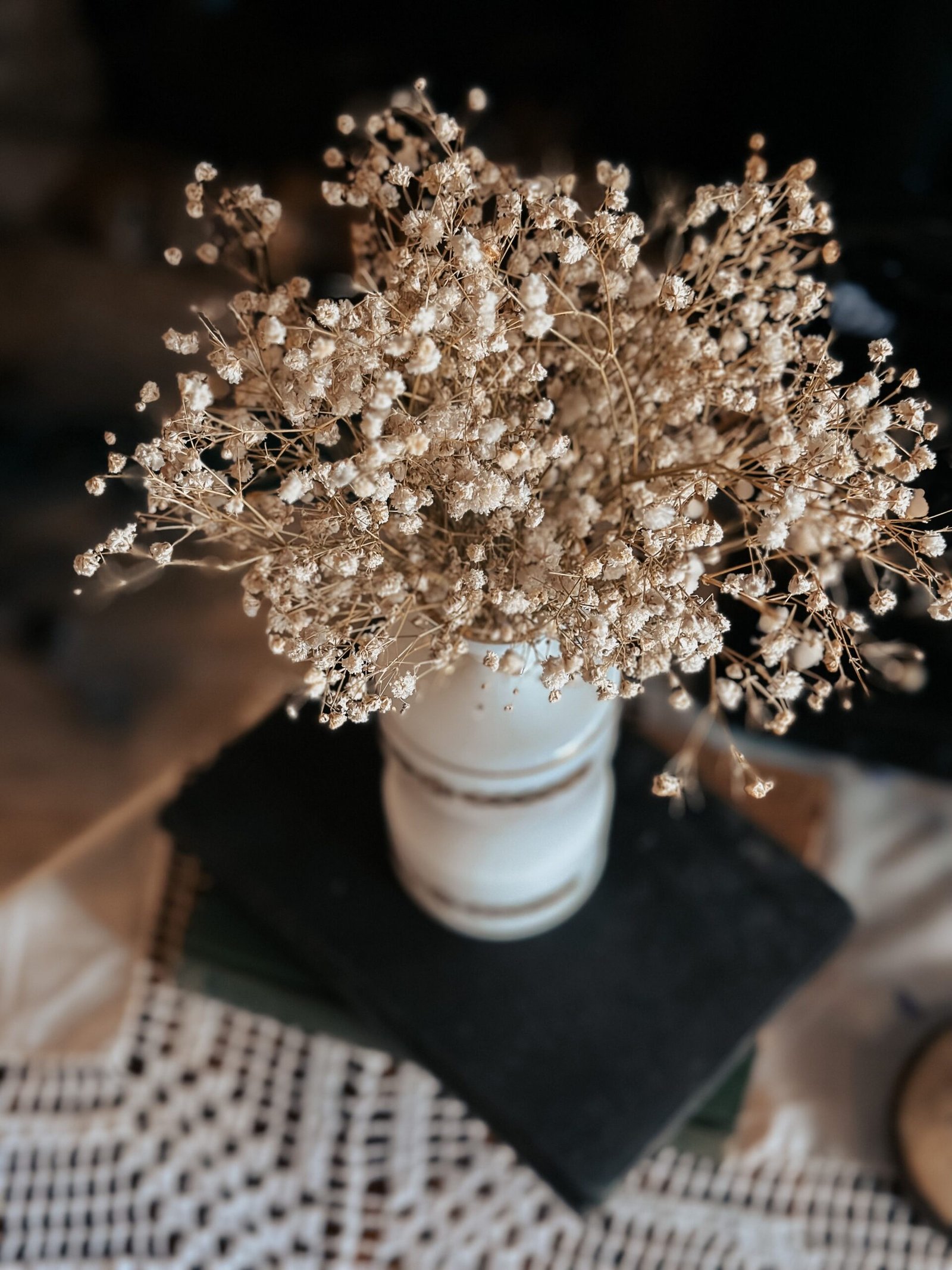 Delicate dried baby's breath flowers arranged in a rustic white vase on a lace-covered table.